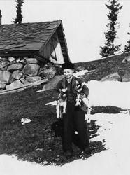 Gutt med to geiter under armene utendørs, ukjent sted.
Seri