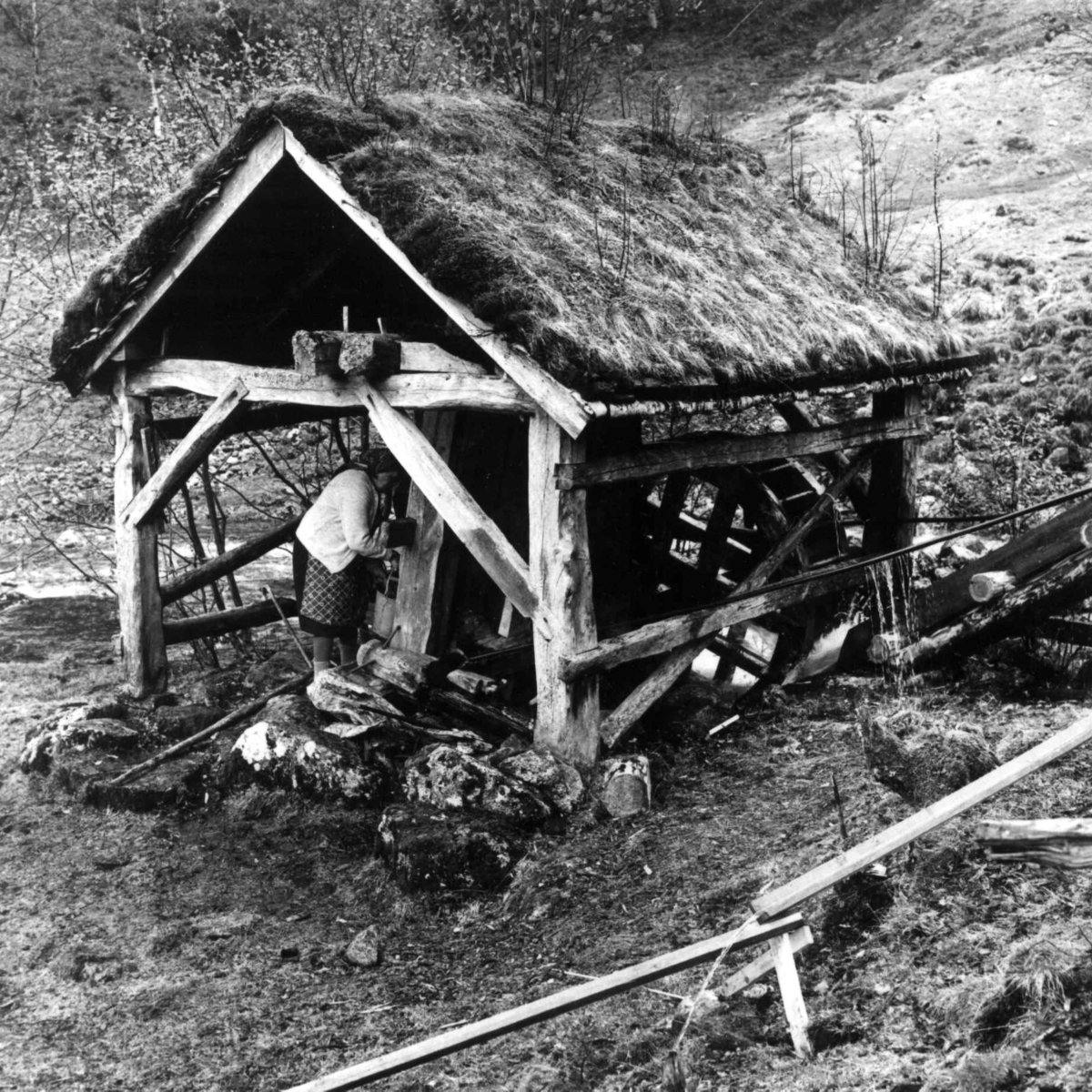 Stamping av vadmel. Serina Kvæstad i stampehuset med vannrenne, i forgrunnen vannrenne til gryte med varmt vann. Kvæstad, Suldal, Rogaland 1970.