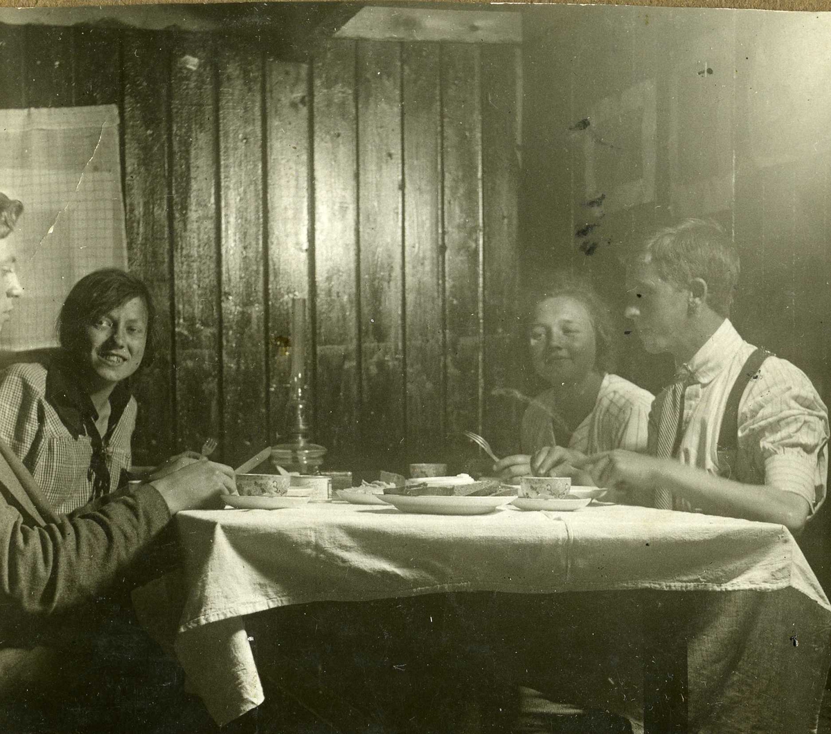 Måltid. To menn og to kvinner sitter ved et bord og spiser med kniv og gaffel og kaffekopper, ca 192