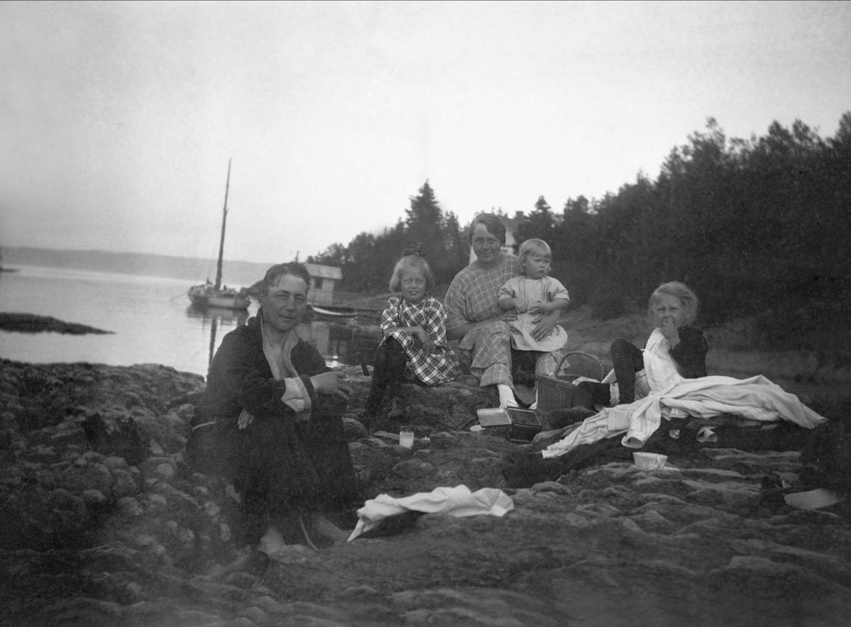 En mann, en kvinne og tre barn raster ved sjøkanten. Robsahm og Lund.