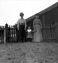 Gruppeportrett, to kvinner og et barn ved et stakittgjerde. 