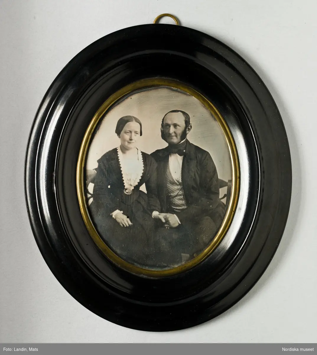 Porträtt av par, föreställer Adolf Sebastian von Krusenstjerna, kaptenlöjtnant (1817–1870) och hans hustru Fredrika Charlotta Vougt (1816–1901). Paret sitter i en soffa och håller varandra i handen. På baksidan påklistrad blå etikett med svart text: "Daguerreotyp af M. UNNA, Porträtt-Målare i Götheborg". Oval dagerrotyp / daguerreotyp med profilerad svart träram med gulmetallvulst närmast dagerrotypen, ca. 1855.
Nordiska museet inv.nr 307611.
-
Portrait of Adolf Sebastian von Krusenstjerna (1817–1870) and his wife Fredrika Charlotta Vougt (1816–1901). Quarter-plate daguerreotype in oval frame by Moritz Unna, c. 1855.