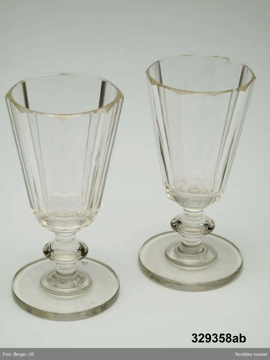 2 st starkvinsglas (a-b) Klart glas, konande facettslipad, åttkantig kuppa. Ben med nod. Rund, plan fot.
Glasen tillhör en typ av helslipade glas som började tillverkas omkring 1830 i Sverige och blev mycket spridda. Ett flertal glasbruk tillverkade denna glasmodell.  Kosta glasbruk har återupptagit tillverkningen av detta glas under namnet Karlberg.
"Glasen inropades på auktion efter familjen Berg på Kymmendö av Oles [givarens] moster, Lisa Wiklund, Dalarö. Glasen ingick i husgerådet i det hus som Strindberg hyrde."
Ur brev från Ann-Marie Söderström till Nordiska museets styresman Christina Mattsson.
2007-01-17 Heidi Henriksson
