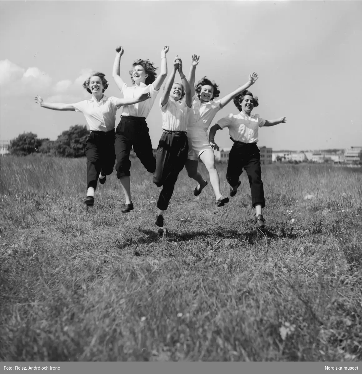Fem flickor hoppar och springer mot kameran på fält.