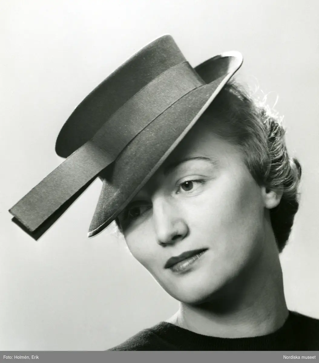 Porträtt av kvinna i hatt med band och uppvikt brätte baktill.
