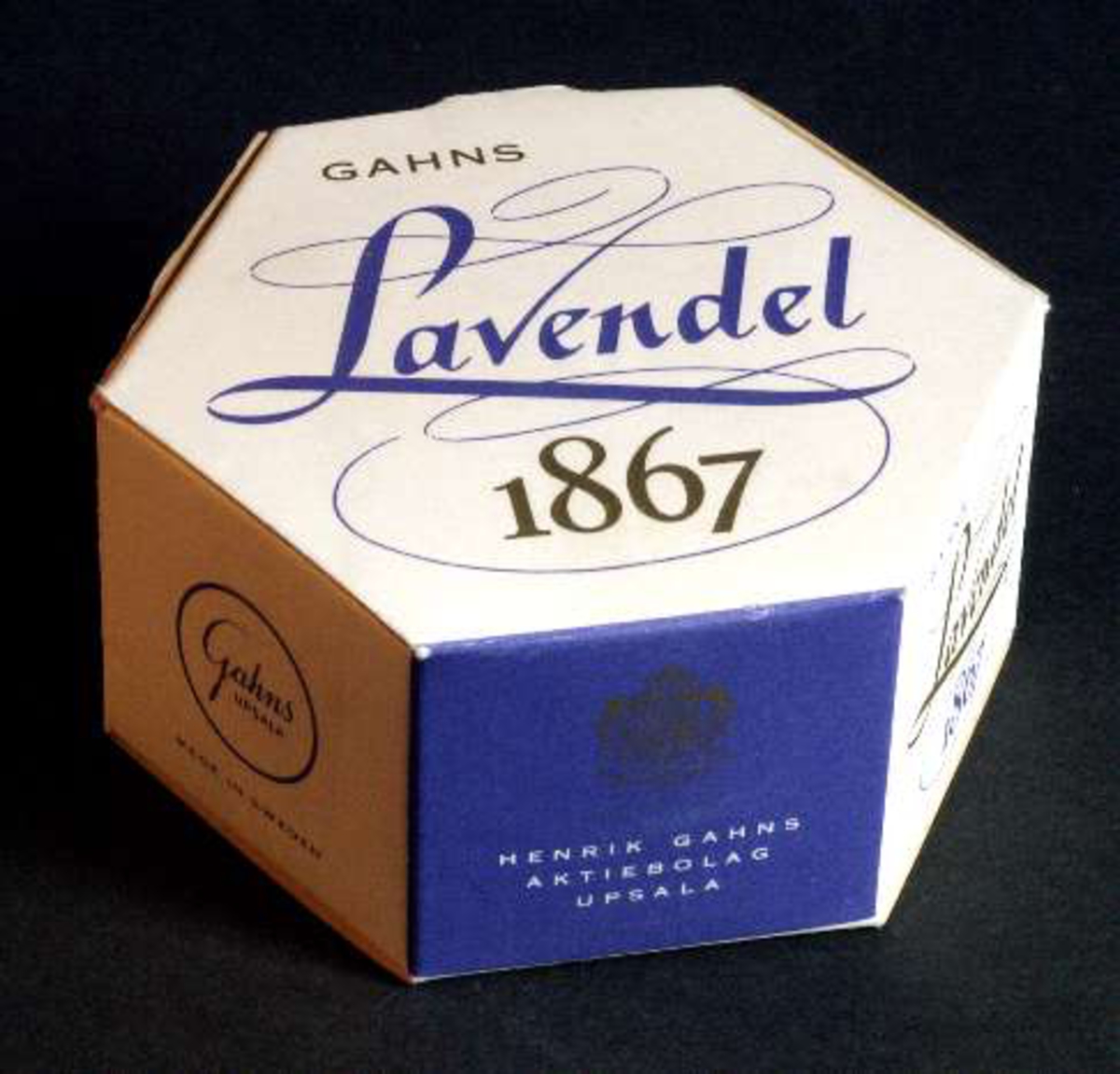 Förpackning med tvål, vit med text i lila och guld "Gahns Lavendel 1867. Henrik Gahns Aktiebolag Uppsala". Innehåller en gulvit rund tvål.