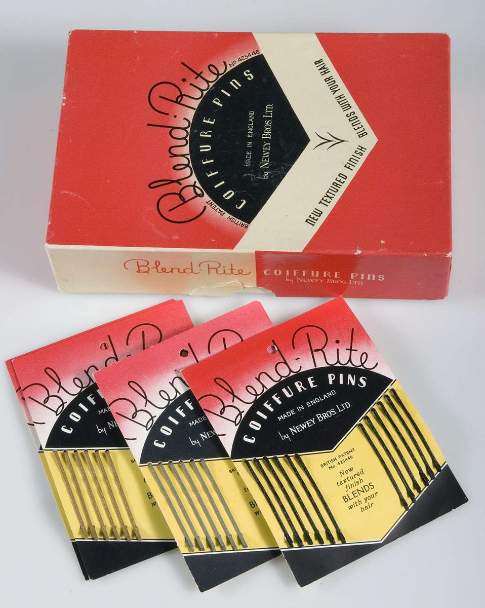 Pappask innehållande hårspännen uppsatta på originalpapper. Förpackningen är röd/vit/svart och innehåller 14 papper med 12 smala hårspännen i två olika färger på varje. På asken tryckt text: Blend Rite COIFFURE PINS. På varje papper tryckt 40 öre.