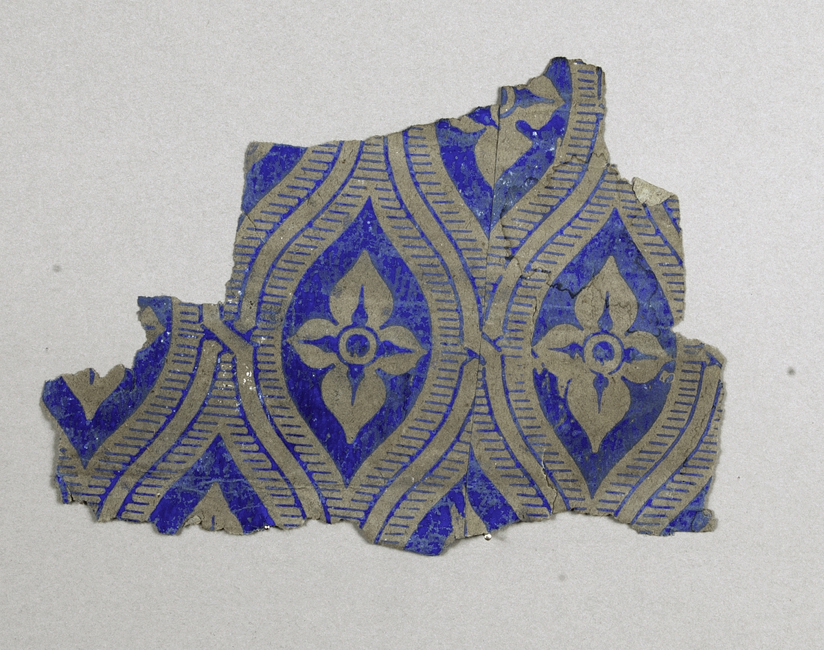 Tapetprovet (3 st. fragment) har brun grundfärg, med tryck i blått. 