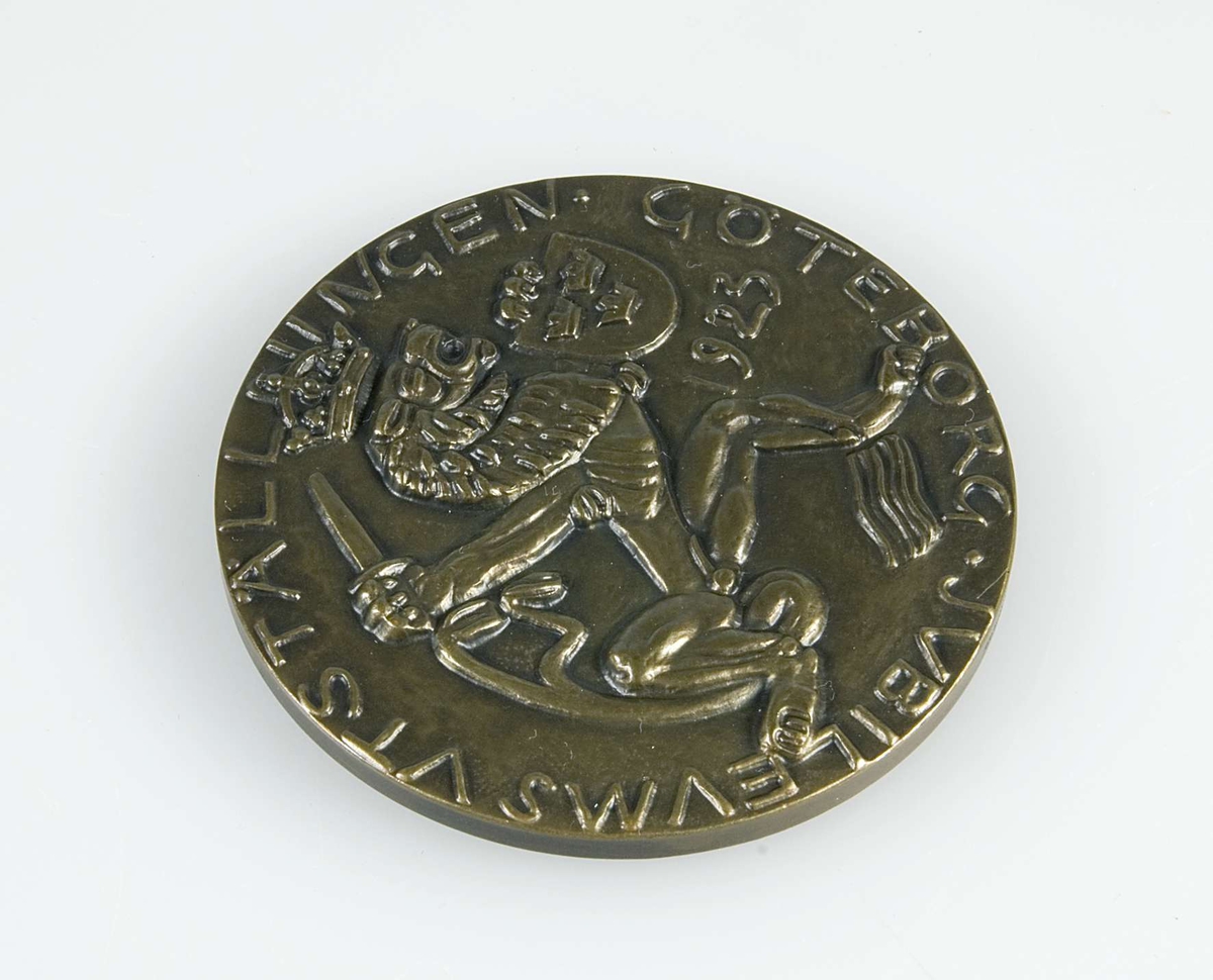 Rund medalj av brons. I relief finns på framsidan texten "JUBILEUMSUTSTÄLLNINGEN GÖTEBORG 1923" samt ett lejon med svärd, krona och sköld med tre kronor. I relief på baksidan finns fyra figurer, sannolikt föreställande gudar, och en delfin. Längs kanten på baksidan står "C. MILLES" med liten text. På sidokanten står "C.C. SPORRONG & CO".