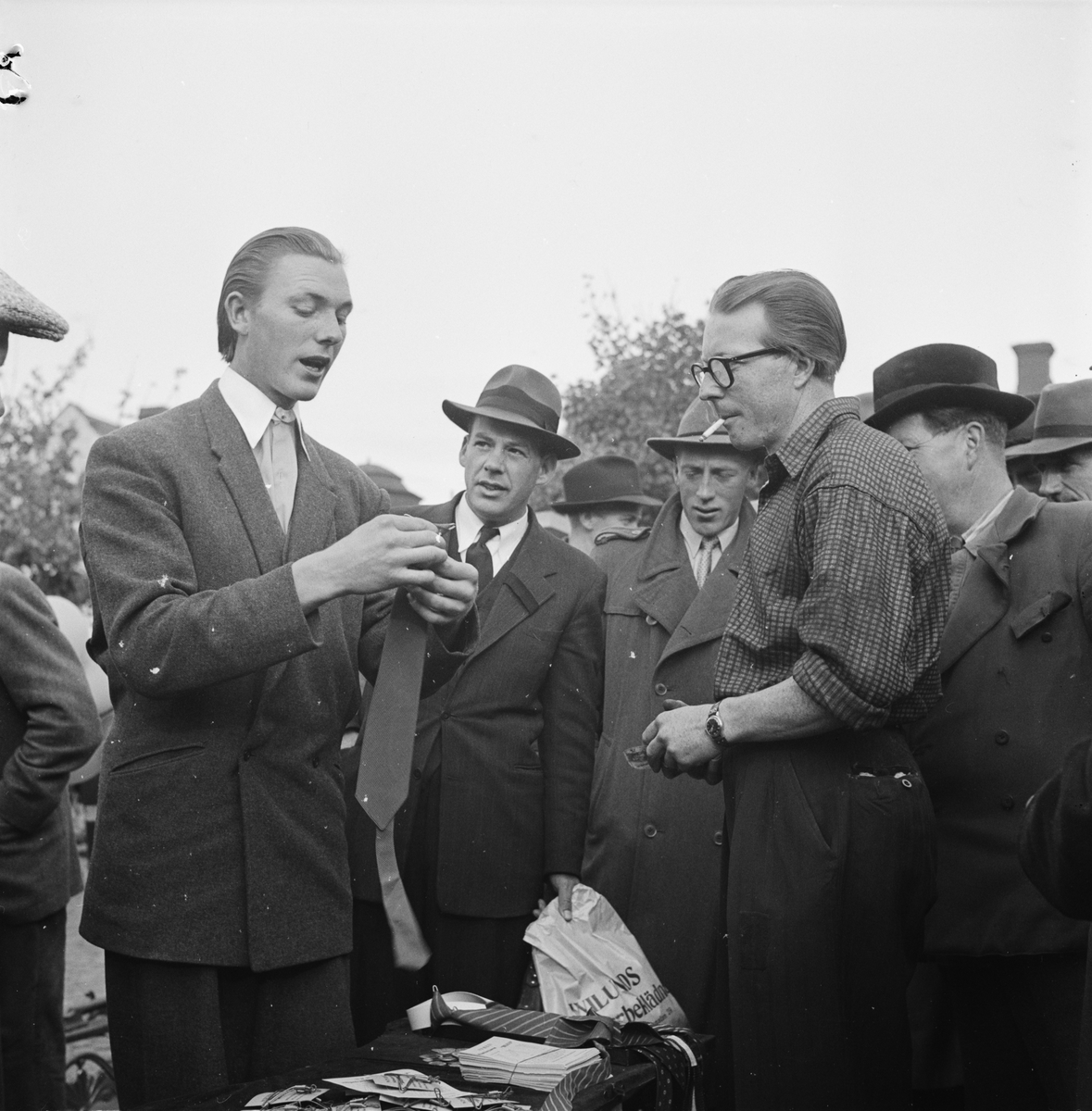 Höstmarknad på Vaksala torg, Uppsala 1948. Bertil Odin "demonsterar hur man behändigt knyter sin slips med hjälp av en ståltrådsställning".