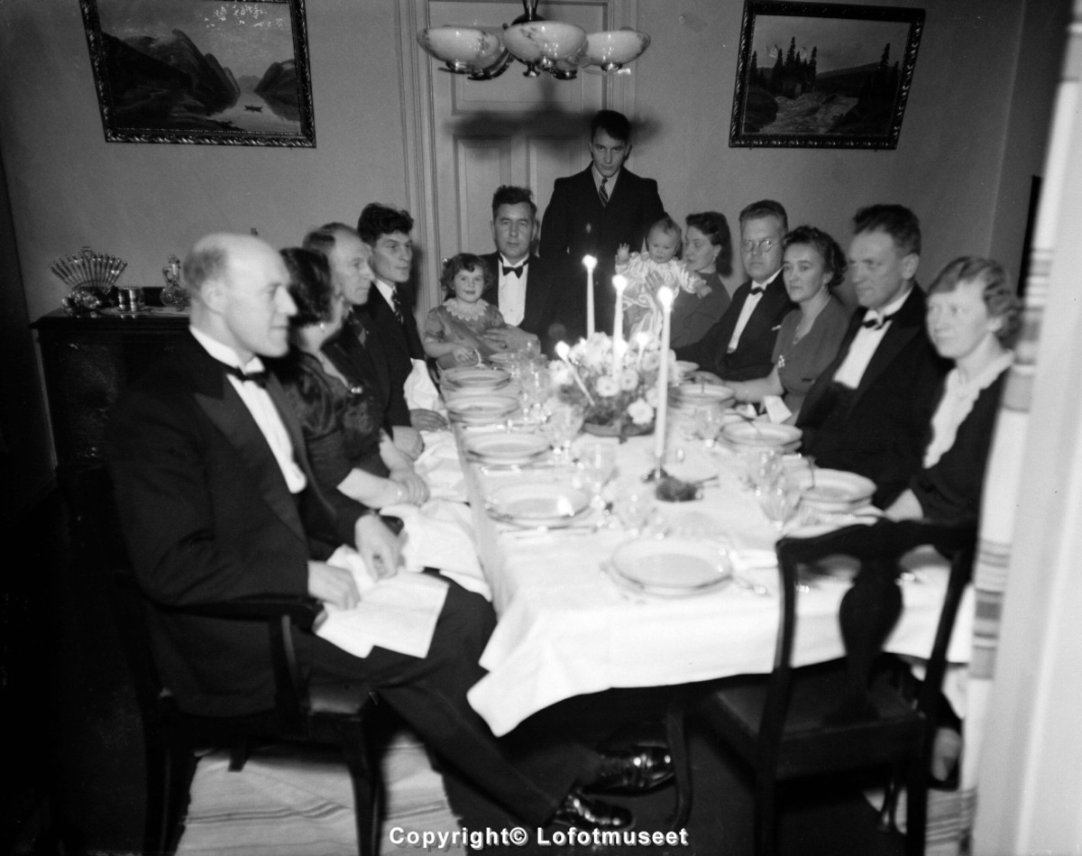 16 personer sitter rundt et festdekket bord i Svolvær, ca. 1950-55.