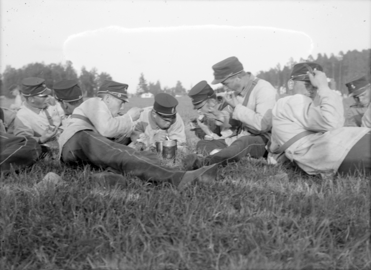 Gruppbild. En samling armésoldater i fält sitter på marken och äter. Soldaterna är antagligen från I 4 och / eller I 5 regemente.