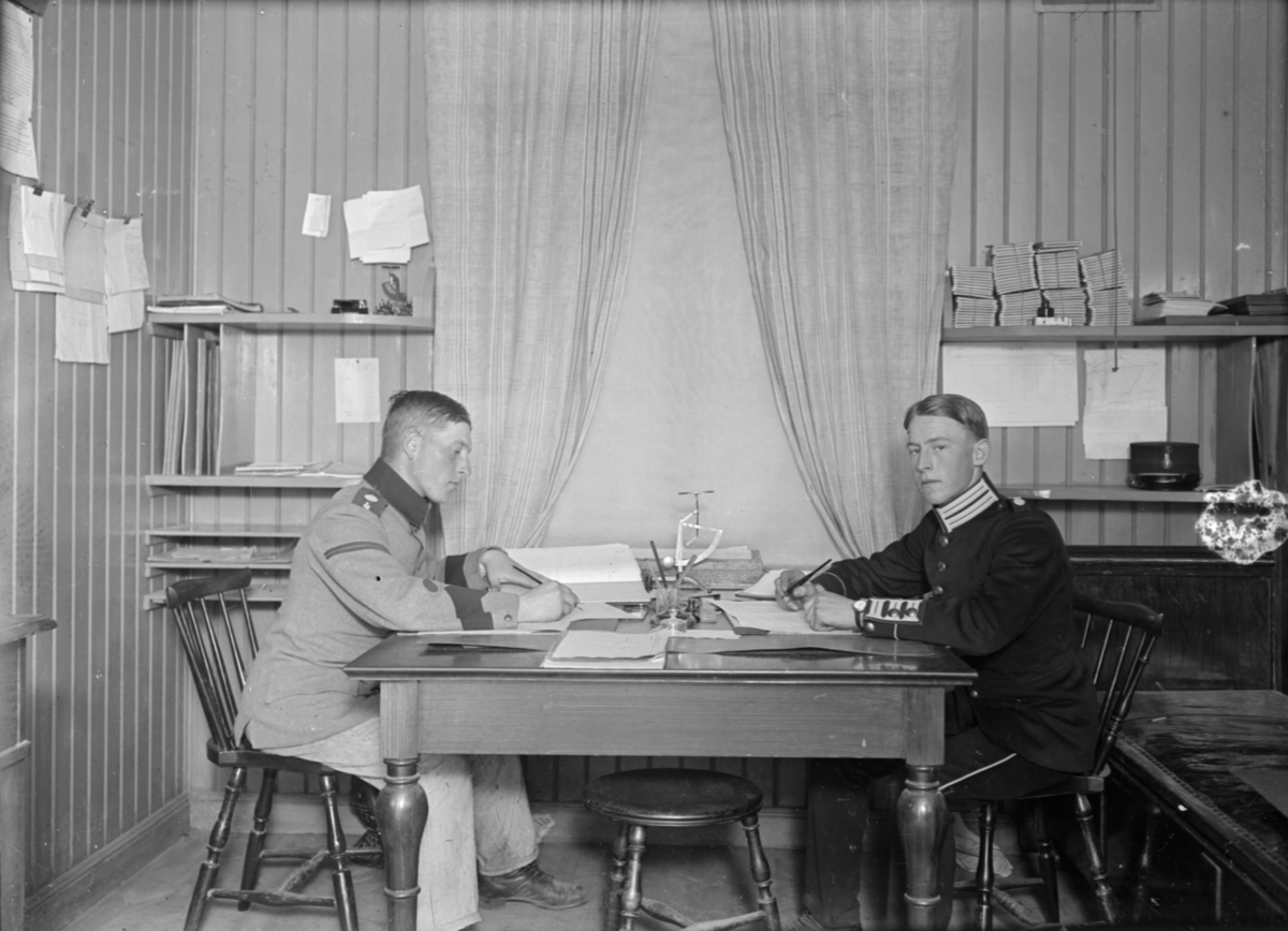 Porträtt. Två armésoldater från I 4 och / eller I 5 regemente sitter vid ett skrivbord. Männen är bröder och heter Henning Axfors (till vänster) och Ernst Axfors (till höger).