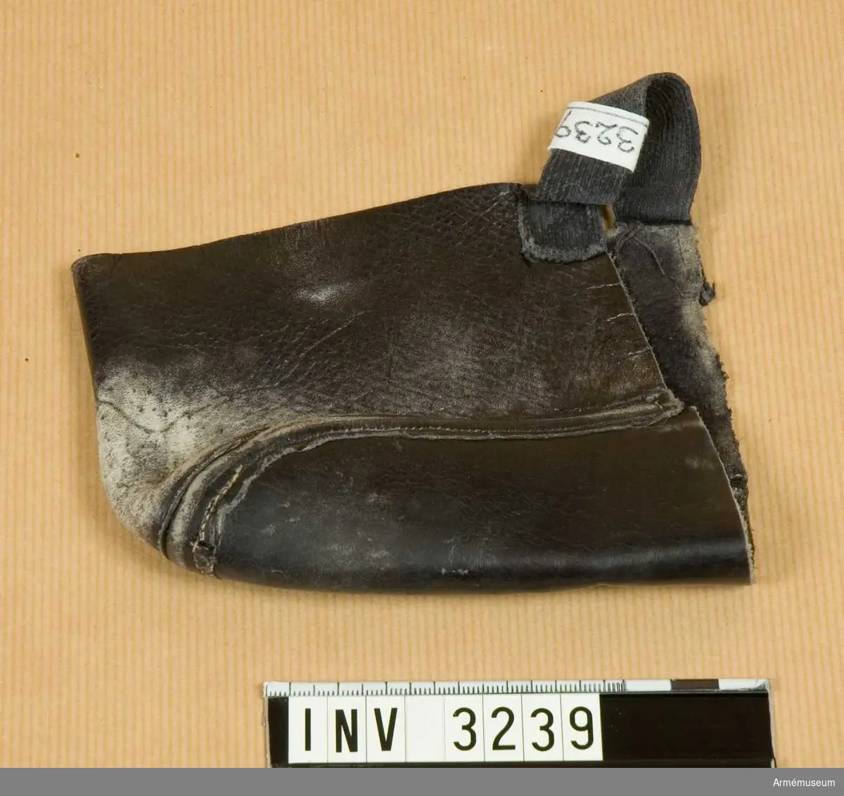 Verkar vara en avskuren sko, typ AM 3238. Av narvat läder. Avskuren vid vristen. Ett påsytt resårband för att hålla fast skyddet.