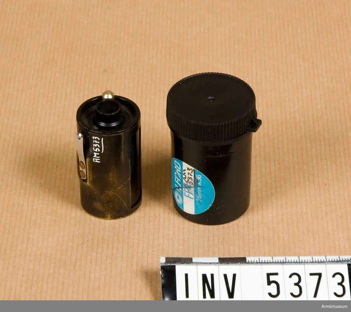 Rullfilmskassett, Leitz. M 7022-210.Kassetten består av en mantel som är dubbel och en spole.  Mörkt brun, en fjäder i krom är skadad. Spolen i svart är troligen av aluminium.Används för 35 mm småbildsfilm som laddas i mörkrum.