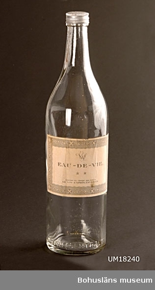 Literbutelj med skruvkork. På en flaska saknas skruvkorken. Etikett för "Eau-de-vie. Importerad och i förskuret skick tappad av Vin & spritcentralen".