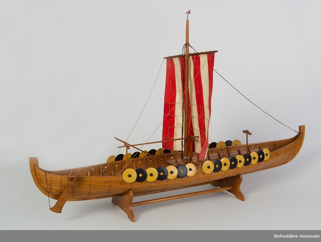 Modell av vikingatida Gokstadskeppet. 
Modellen är riggad och med vit- och rödrandigt råsegel.  Klinkbyggt och lackat träskrov. Längs båtens sidor sitter runda sköldar i svart och gult. 
En av sköldarna har lossnat, annars i gott skick.