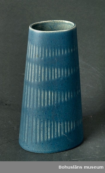 Ovalformad, uppåt konande vas med dekor av räfflade romber. Matt blåglaserad.
Märkt i botten med signatur i relief: SYCO - SWEDEN - 1472.