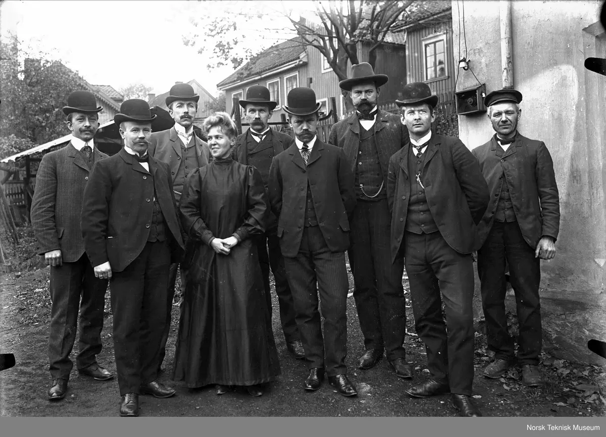 Åtte menn og en kvinne utenfor verkstedet (Ingeniører ved Kampens mekaniske verksted?)