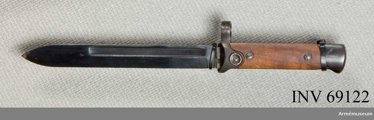 Fällbar knivbajonett m/1915 för flottan, att fästa på karbin.
Eneggad blånerad klinga med blodränna på båda sidor. Fäste av trä. Inristat i fästet: PS inuti en cirkel. H 95875, stämpel oklart vad.