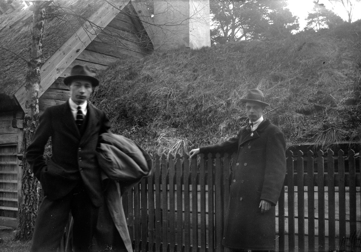 Jönköpings Stadspark. Två män, till vänster Gustav Andersson, står vid ett staket vid Ryggåsstugan hämtad från Sjöaryds by, Markaryds socken, Sunnerbo härad.