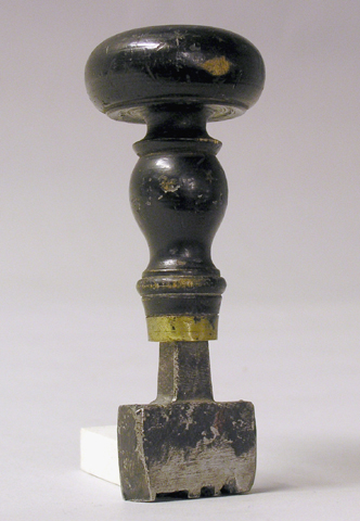 Stämpel, med stamp av stål, träskaft med mässingsring.
Avrakstämpeltyp utan ram. Avtryckets mått:31x9 mm.