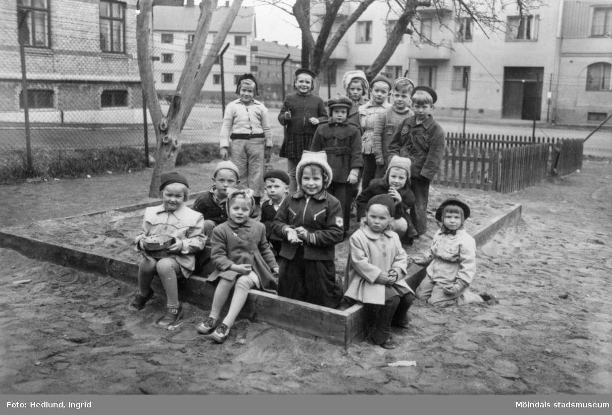 Några barn som står i en sandlåda uppställda för fotografering. Okänd plats 1945-.