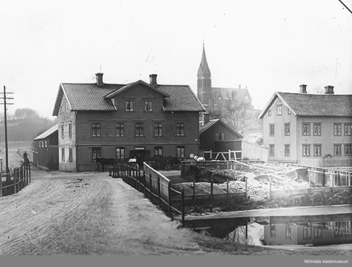 Gamla Mölndalsbro innan spårväg och stensättning tillkom i området. Fässbergs kyrka ses i bakgrunden. Före 1900-tal.