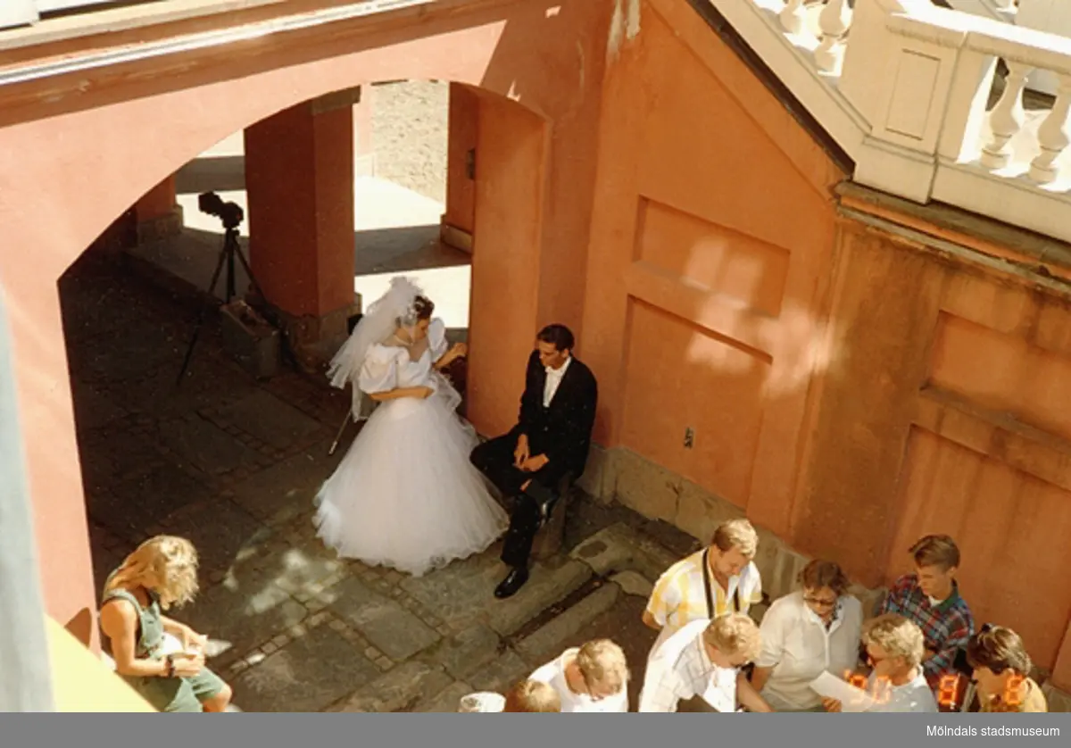 Till vänster ses ett brudpar som pratar. De befinner sig i valvet nedanför Gunnebo slottsterrass. Till höger står andra personer och tittar i papper, augusti 1990.
