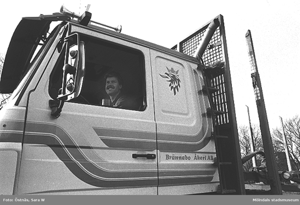 En chaufför sitter i en lastbil märkt "Brännabo Åkeri AB", 1980-tal.
Bilden ingår i serie från produktion och interiör på pappersindustrin Papyrus.