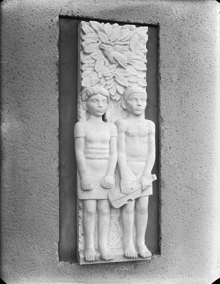 Relief på en fasad med en flicka och en pojke med fiol