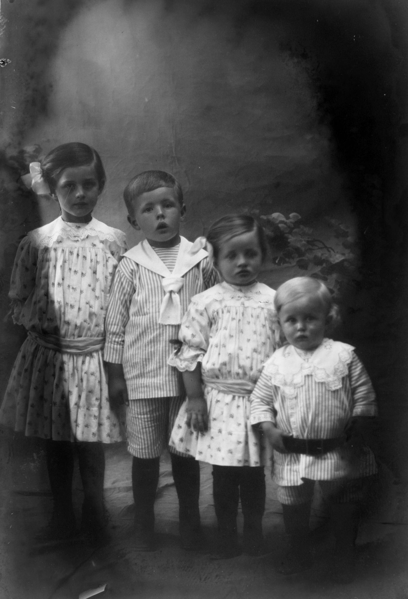 Studioportrett av fire barn som er stilt på en rekke etter alder, med eldste til venstre og yngste til høyre.