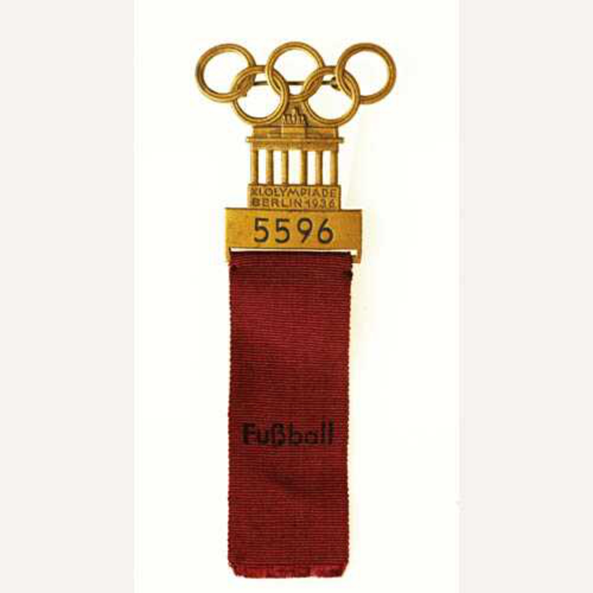 Metallspenne med Brandenburger Tor og olympiske ringer. Rødt bånd med "Fussball" under.