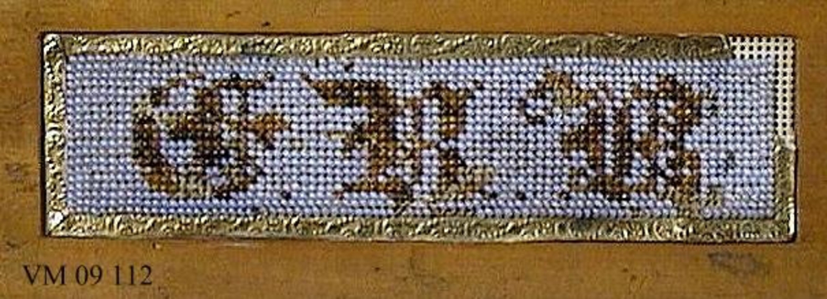 En trälinjal med infällt pärlbroderi i vita och svarta pärlor.

Broderiets mått: L. 11 cm.  B. 3 cm.