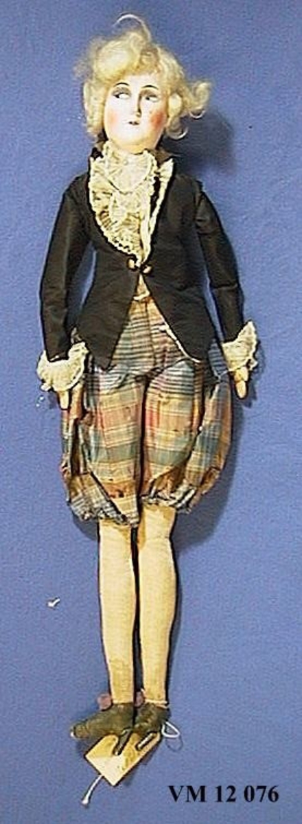 långsmal docka av ''1700-tal modell'' iförd  puffbyxor av rutigt siden (trasiga), svart jacka med krås under, högklackade skor av skinn. Kroppen av stoppat tyg.