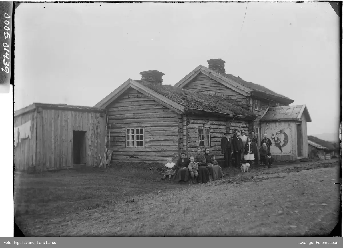 En gruppe mennesker foran en tømmerbygning med torvtak..