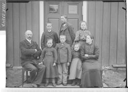 Gruppebilde av mann, kvinne og seks barn foran et inngangspa