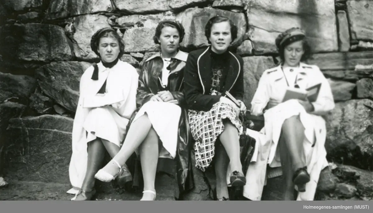 Fire jenter med russelue sitter ved en steinmur.