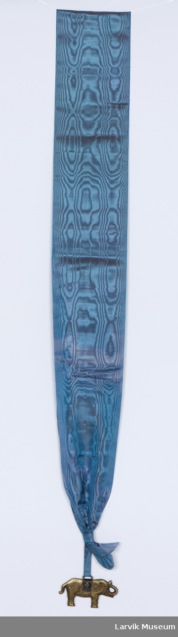 Form: messingelefant i turkisblått moiré-bånd med sløyfe
