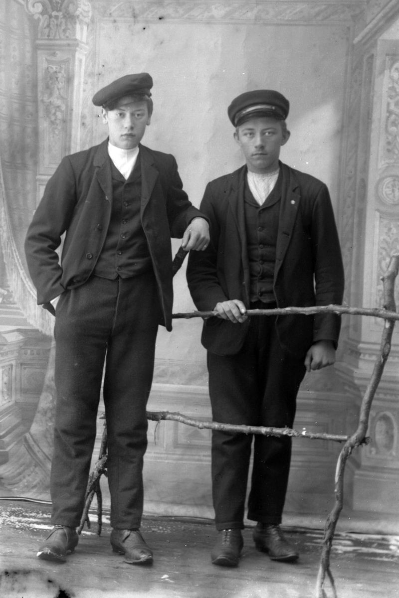 Studioportrett av to unge menn posert med et gjerde.