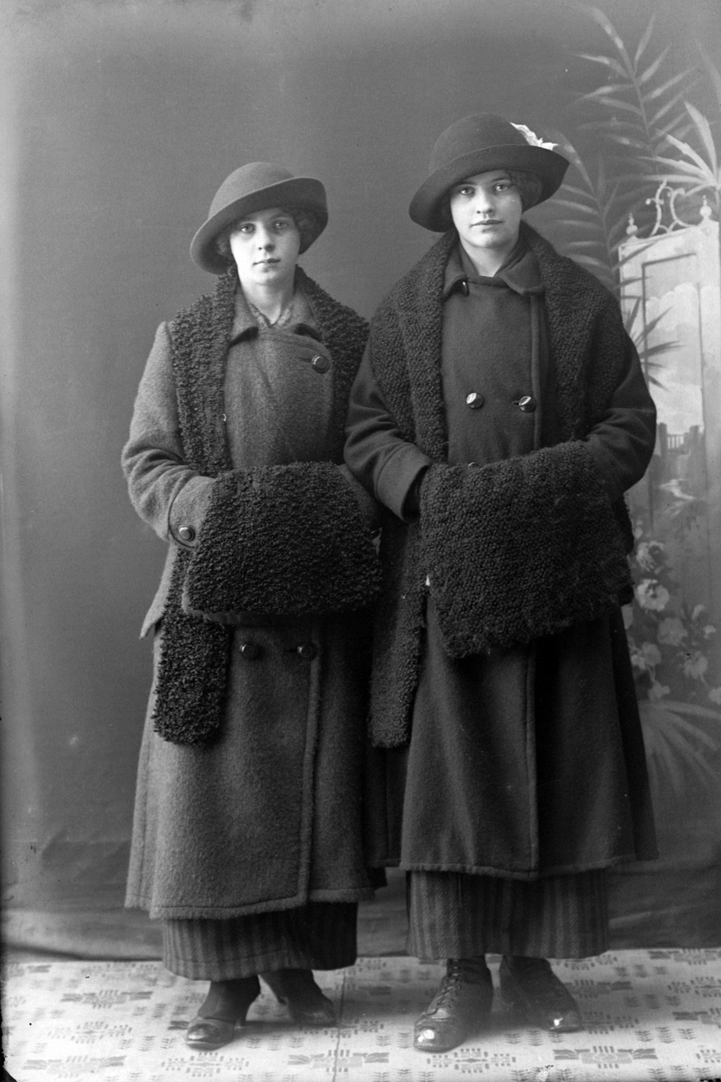 Studioportrett av to kvinner med to hatter og muffer.