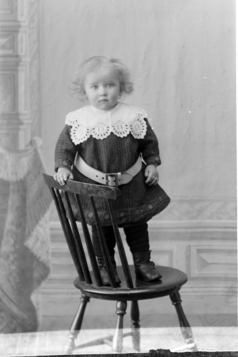 Studioportrett av et barn som står på en stol.