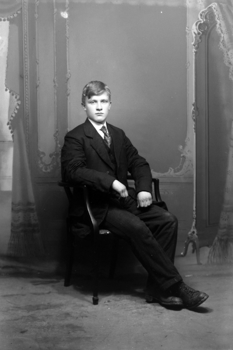 Studioportrett av ung mann, sittende i en stol.
