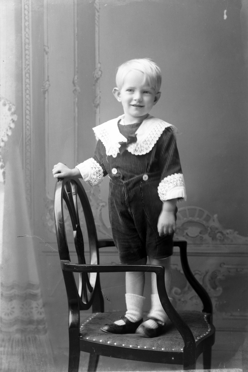 Studioportrett av en ung gutt stående på en stol.