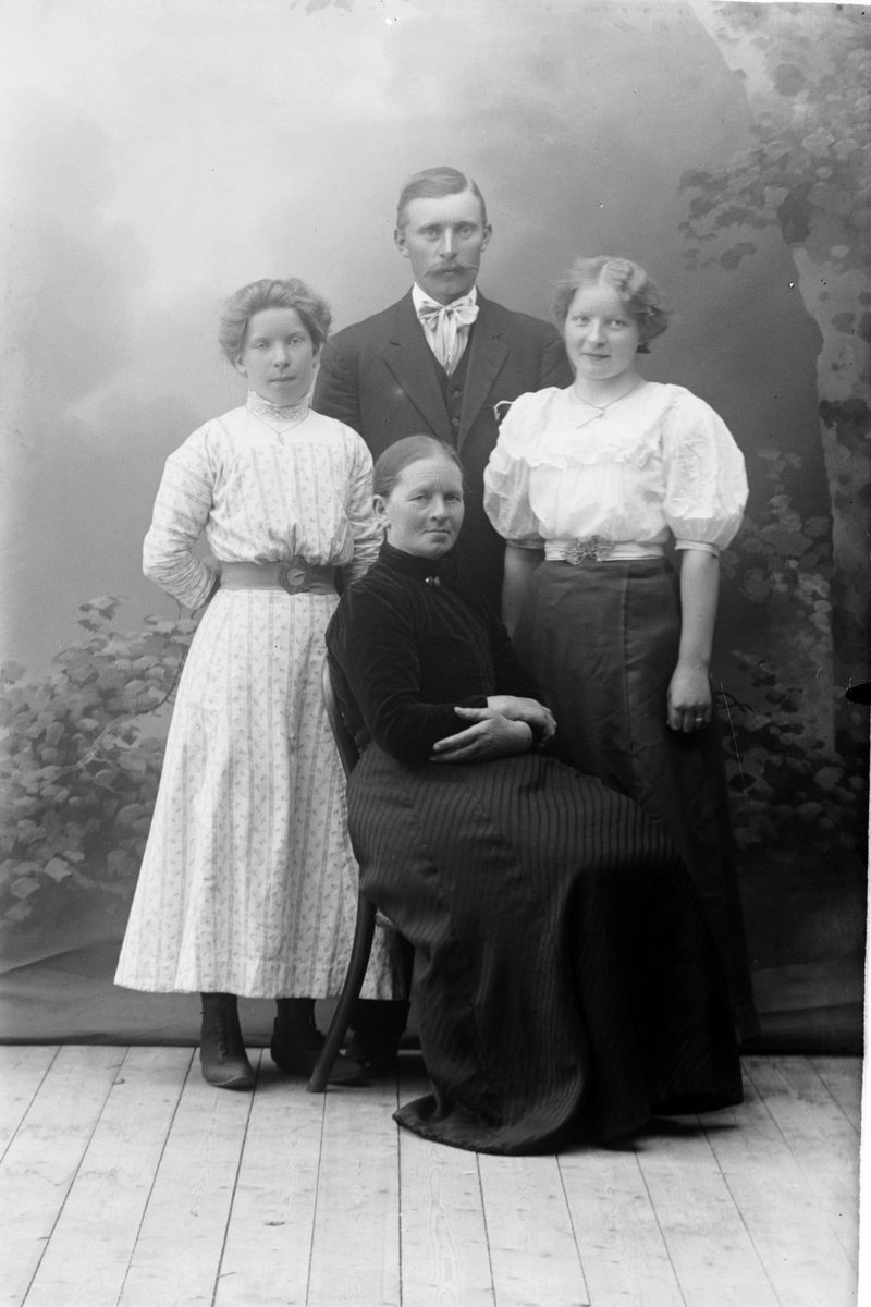 Studioportrett av en mann omgitt av tre kvinner.