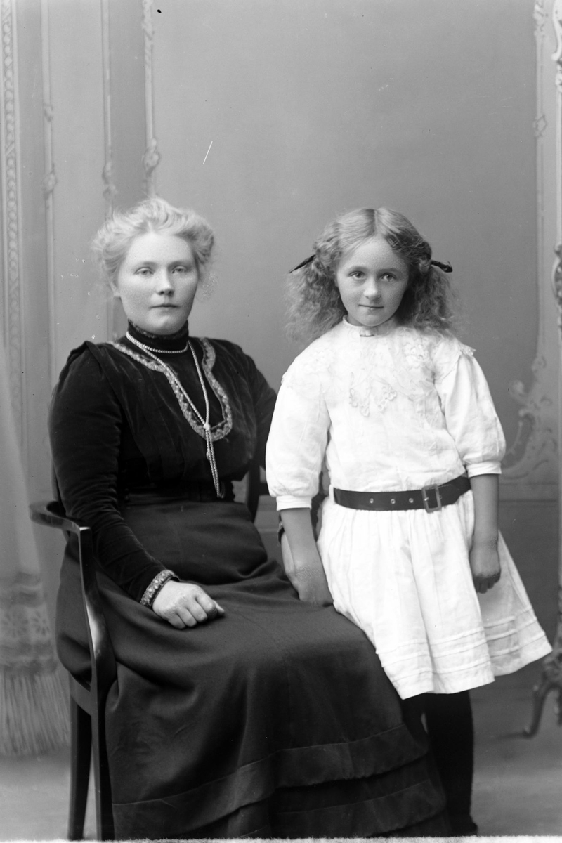 Studioportrett av en kvinne sittende ved siden av en ung pike.