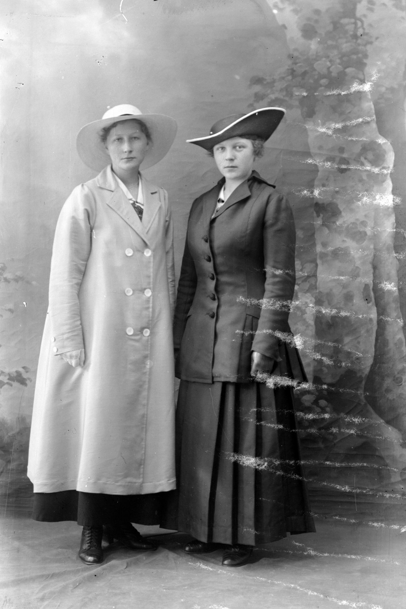 Studioportrett av to kvinner med store hatter på hodet.