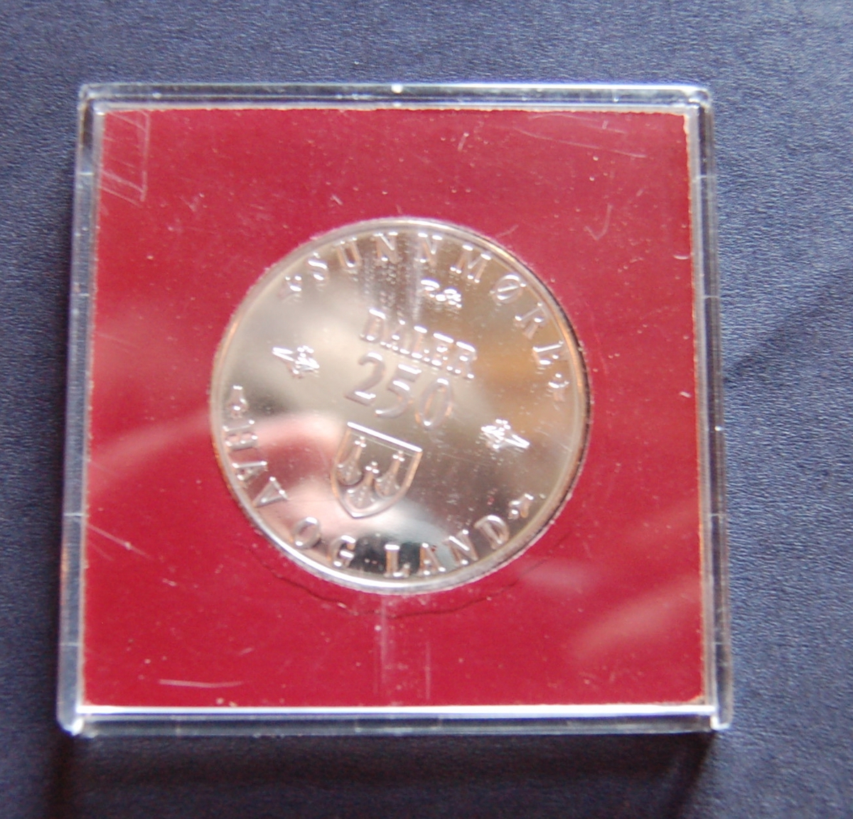 Form: Rund mynt i kvadratisk etui av tre
