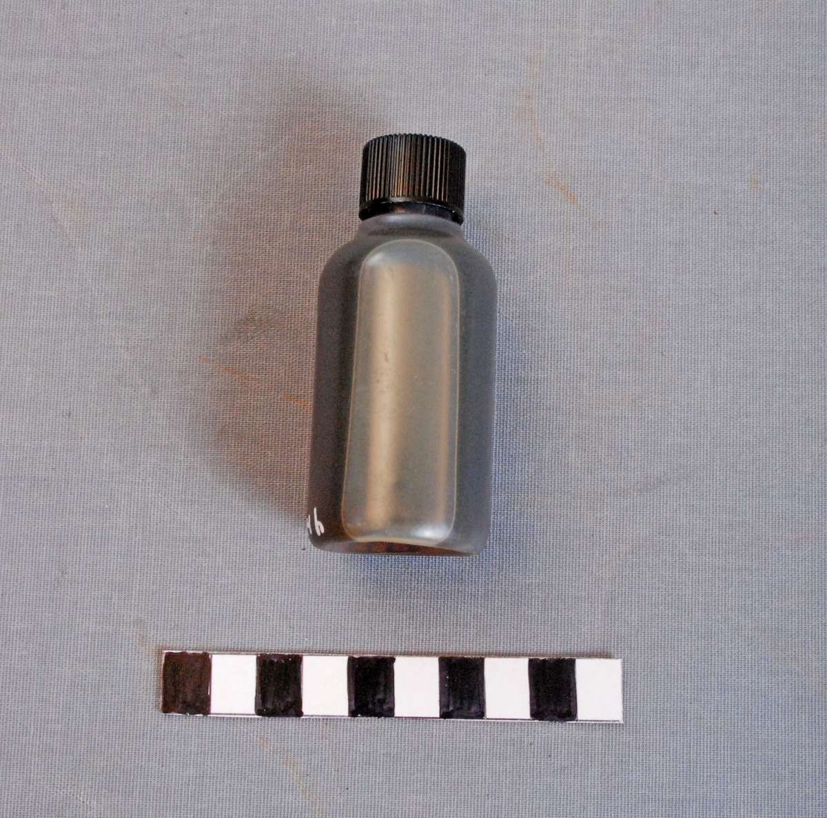 Oljeflaske for bruk til linepistol/redningspistol. Flasken er sylindrisk og har svart plastkork. Inneholder olje.