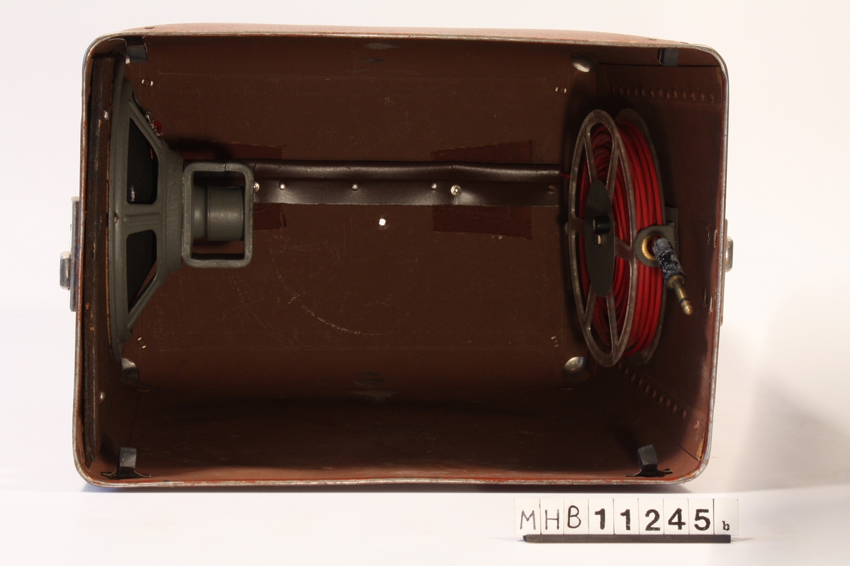 Etui til smalfilmframviser med innebygd høytaler. Stor brun boks til å oppbevare framviseren i. Det er innebygd høytaler i boksen som kan kobles til framviseren. Ledning er festet på innsiden.